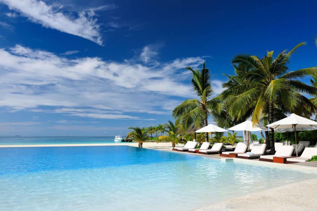 Blue skies and a beach hotel with cabanas, a pool, and the ocean in the background.