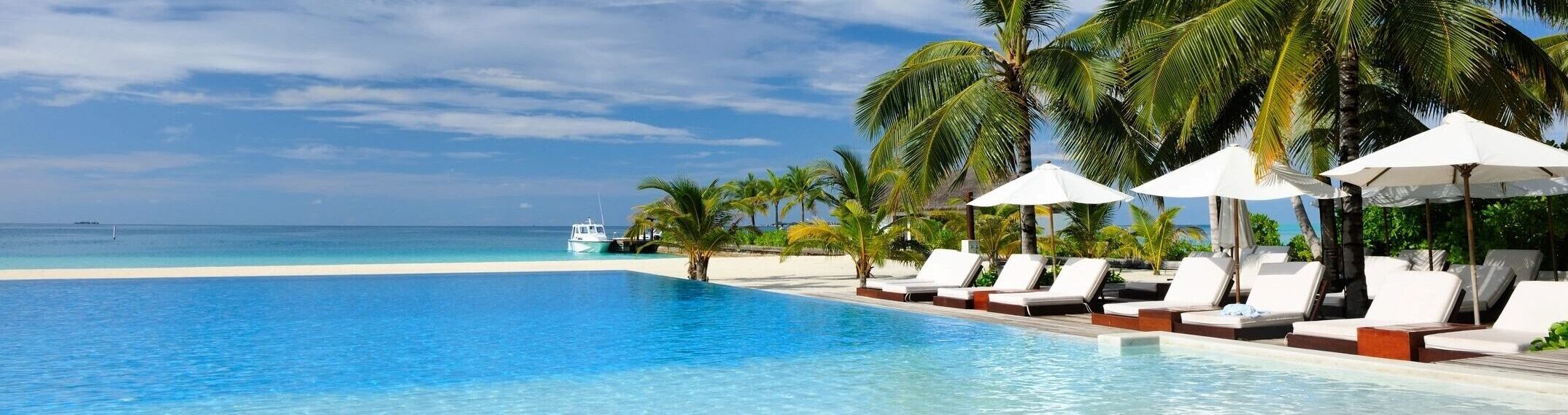 Beautiful hotel with an oceanside pool and white cabanas and palm trees.